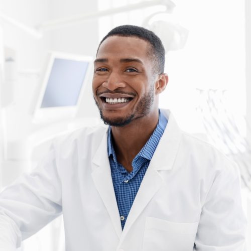 Handsome black young man dentist smiling over modern dental clinic background