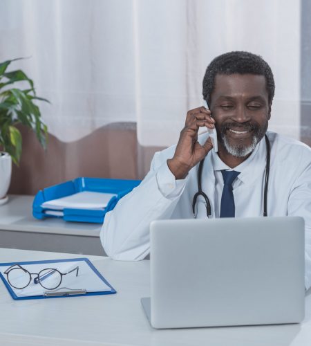 Smiling african american doctor sitting at the table and talking by smartphone
